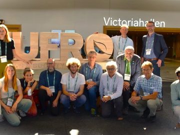 Gruppenbild der REGULUS-Teilnehmenden vor dem mannshohen IUFRO Holzlogo und Treffpunkt vor den Victoriahallen der IUFRO Weltkonferenz © Andy Selter